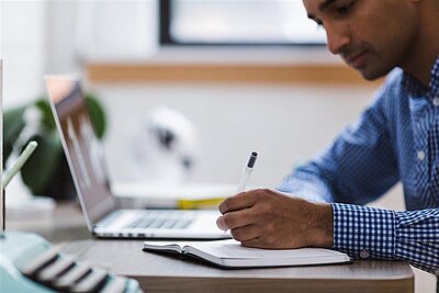 man sitting at desk writing on a notepad