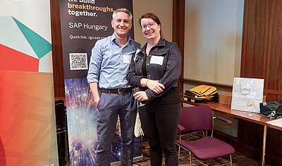 Birgit Fuhrmann and Frank Kimmerle standing in front of the sponsor SAP's rollup banner 