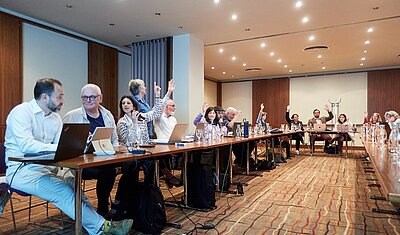 tekom Europe Assembly in a conference room with attendees putting up their hands for vote
